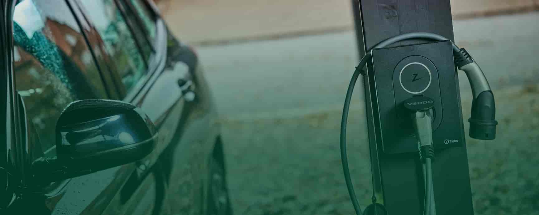 kvinde står med mobil mens elbil oplader